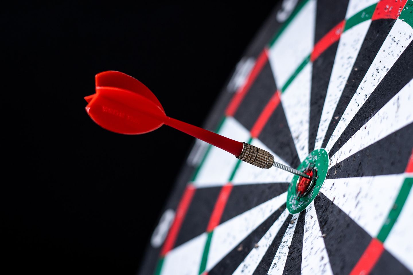 Ein roter Dartpfeil steckt genau im Bullseye einer klassischen Dartscheibe.