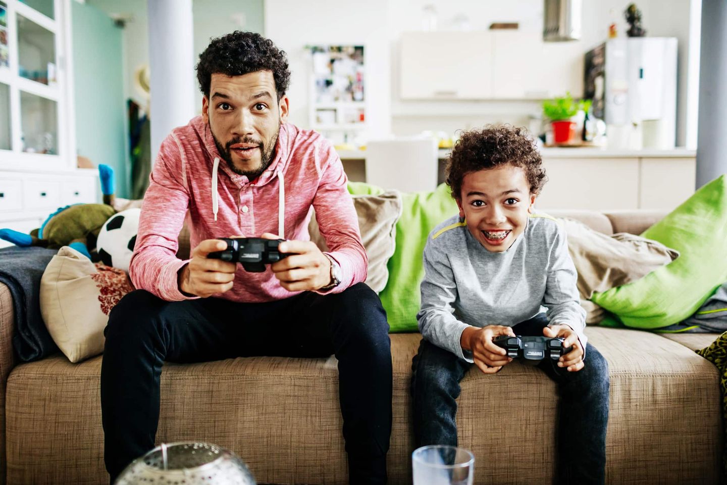 Vater und Sohn sitzen auf dem Sofa und spielen zusammen Videospiele. Getty