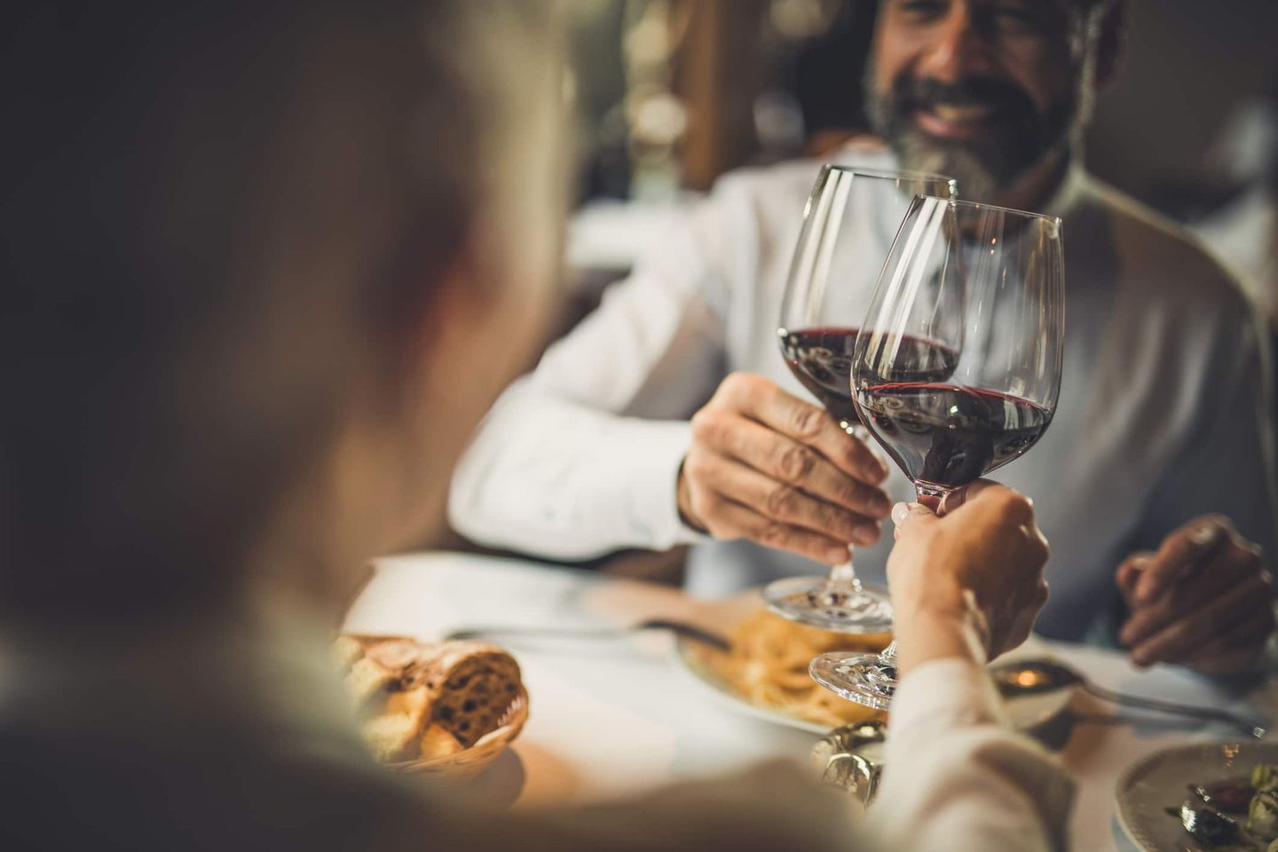 Zwei Personen stoßen mit Rotweingläsern im Restaurant an. Getty