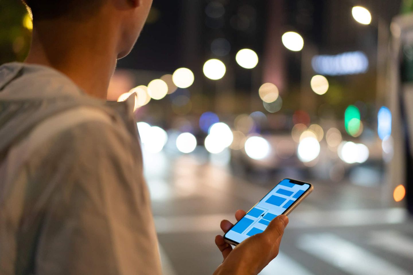 Person mit Smartphone in der Hand, nachts auf einer belebten Straße mit unscharfen Lichtern. Getty