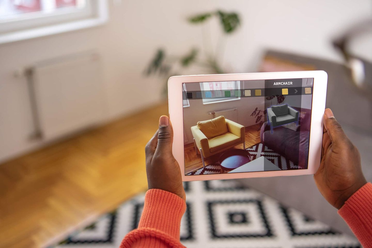 Person hält ein Tablet mit Augmented-Reality-App zur virtuellen Möbelauswahl in einem Wohnzimmer. Getty