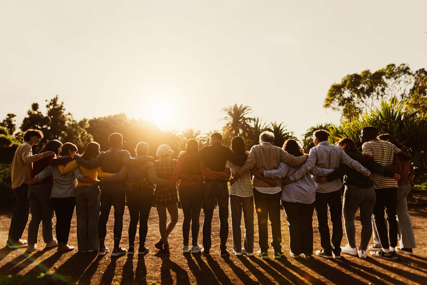 Eine Gruppe von Menschen steht Arm in Arm in der Natur und schaut gemeinsam in den Sonnenuntergang Getty