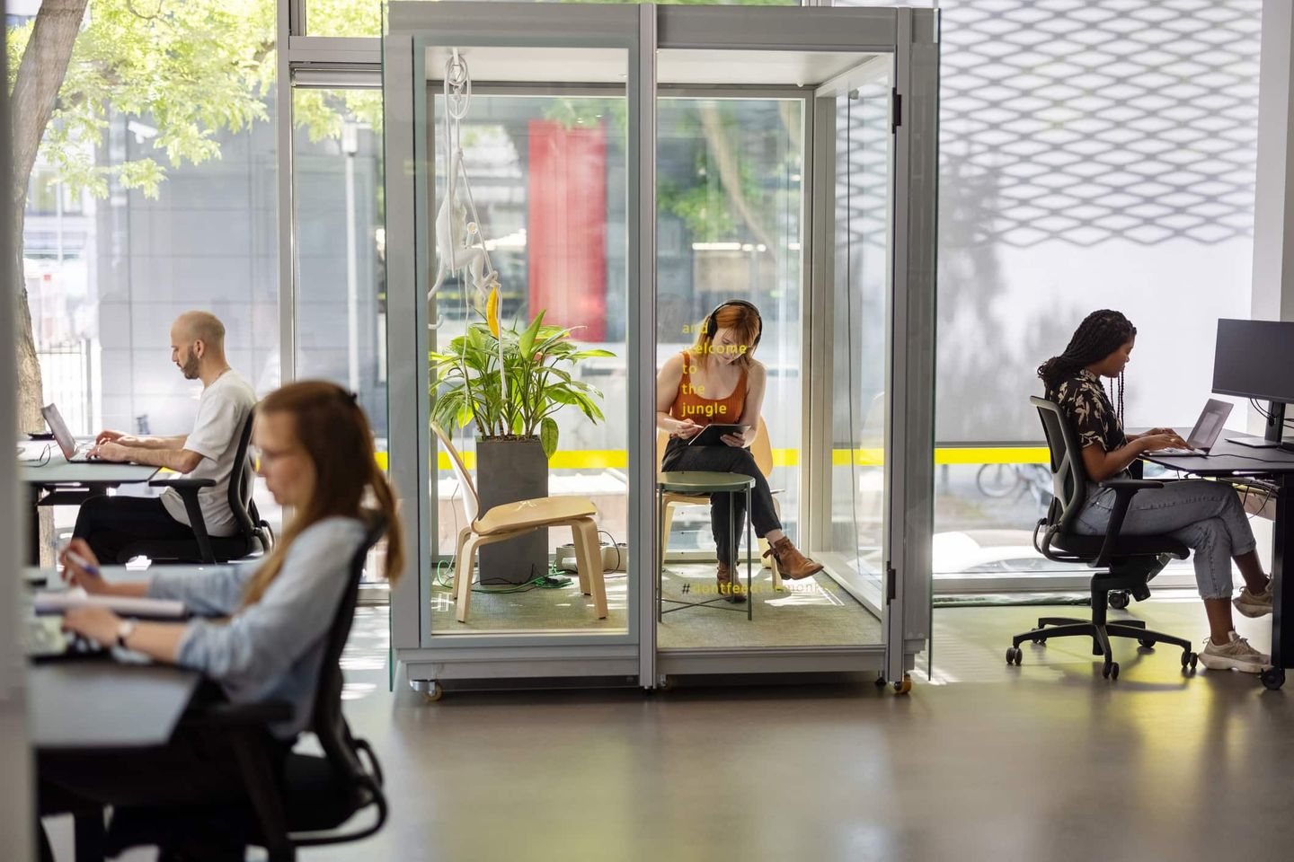 Menschen arbeiten in einem modernen Großraumbüro mit Glasboxen für konzentriertes Arbeiten Getty