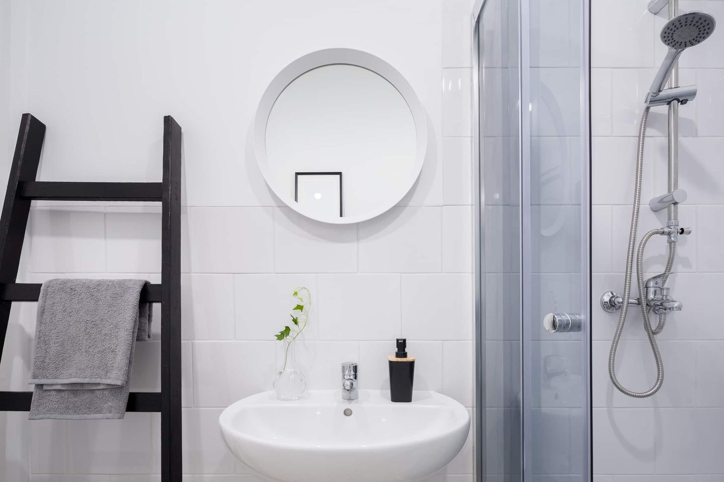 Modernes kleines Badezimmer mit Leiterregal, rundem Spiegel und Dusche. Getty