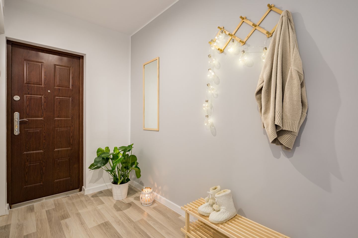 Gemütlicher Flur mit Holztür, kleinem Spiegel, Pflanzen, Lichterkette und Holzbank mit Hausschuhen