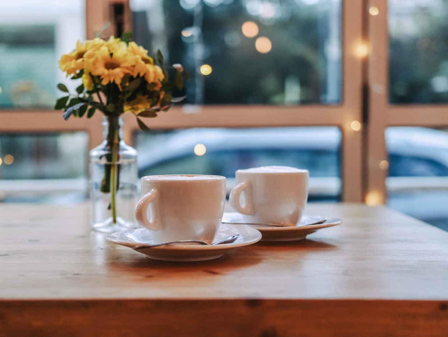 Zwei Cappuccinos auf Holztisch mit Blumenstrauß im Café Getty