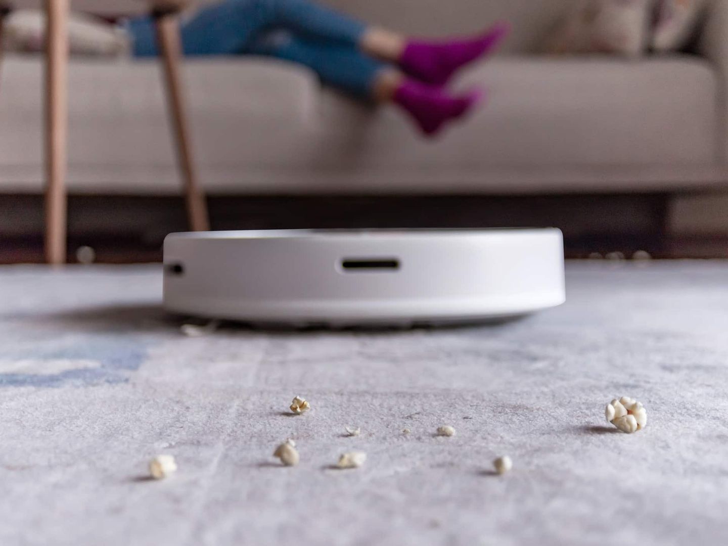 Staubsaugerroboter reinigt Krümel vor Sofa mit sitzender Person