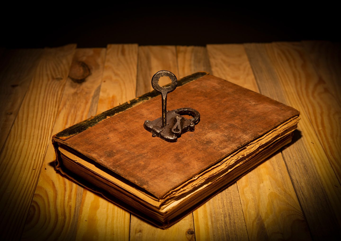 Ein altes, abgegriffenes Buch mit bräunlichem Einband liegt auf einem Holztisch. Auf dem Buch liegt ein antikes Schloss mit einem passenden Schlüssel.