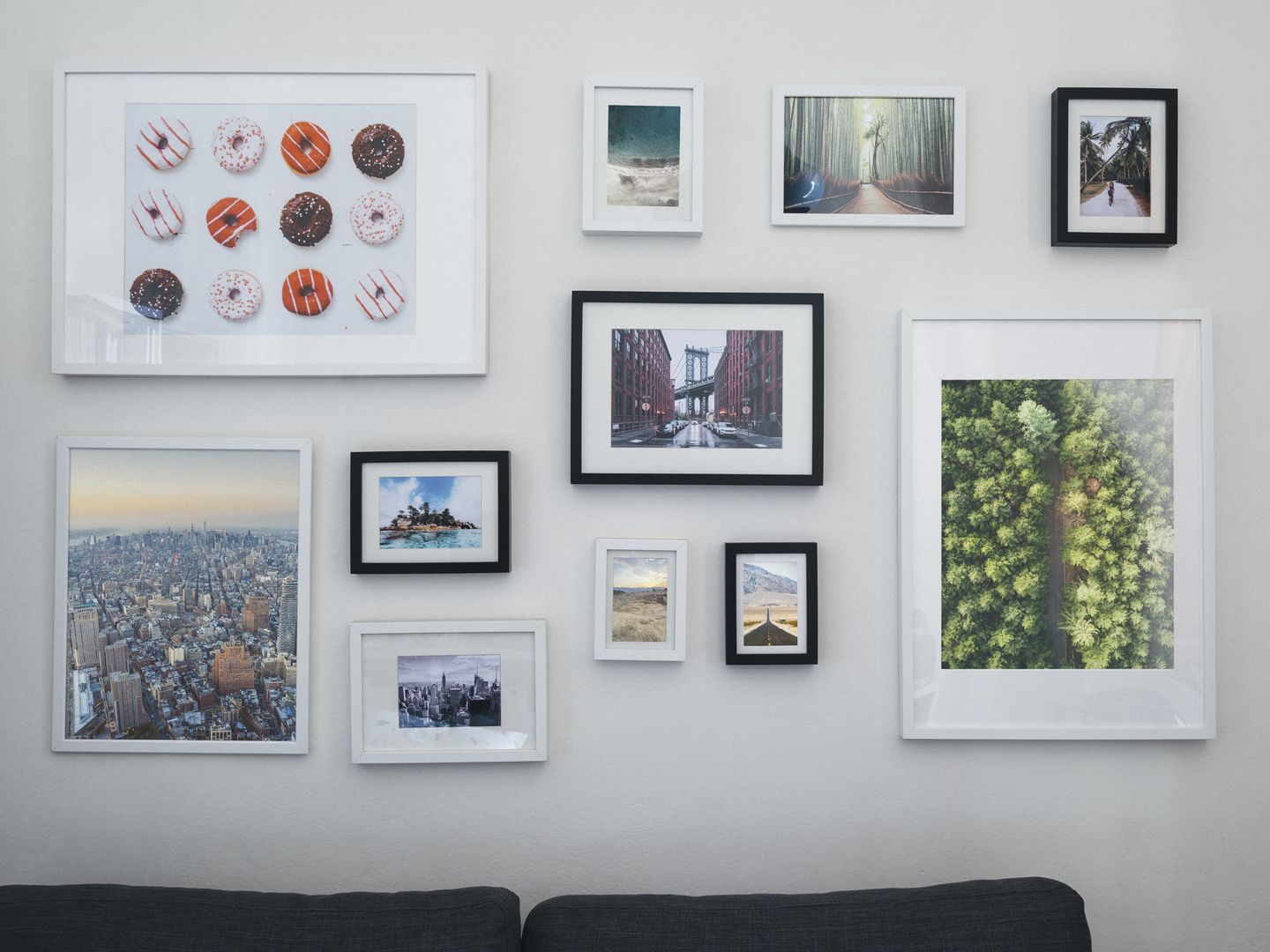 Wand mit einer Galerie aus verschiedenen gerahmten Fotos und Bildern, darunter Stadtansichten, Landschaften, ein Donut-Motiv und Naturaufnahmen