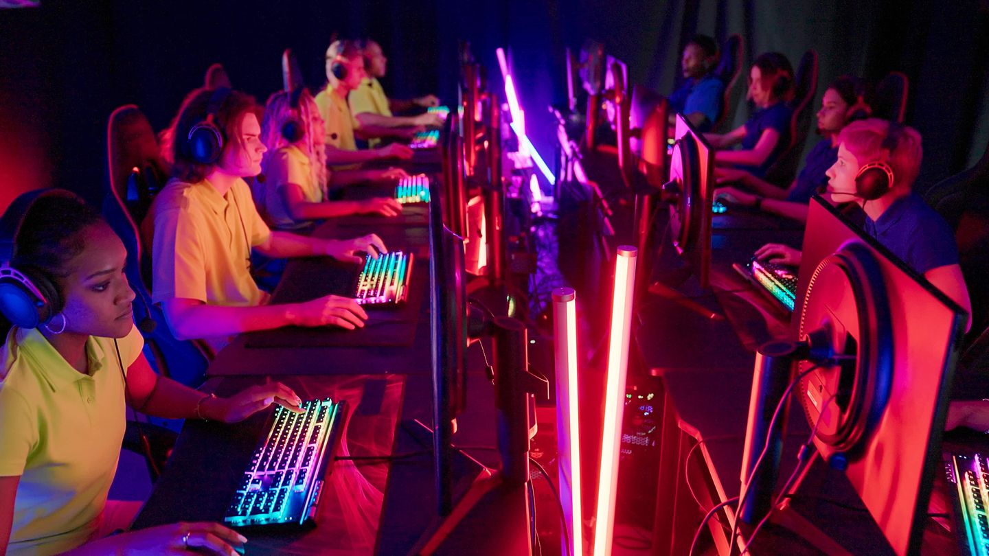 Gruppe von Jugendlichen spielt in einem eSports-Raum an Computern mit Neonbeleuchtung.