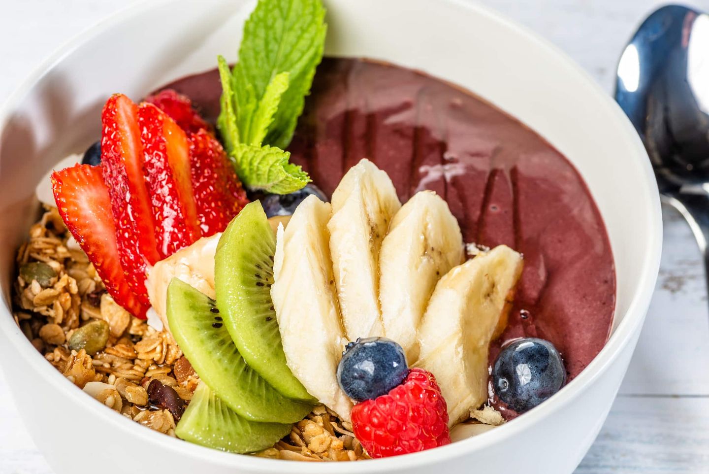 Bunte Smoothie-Bowl mit Früchten, Granola und Minze garniert. Getty