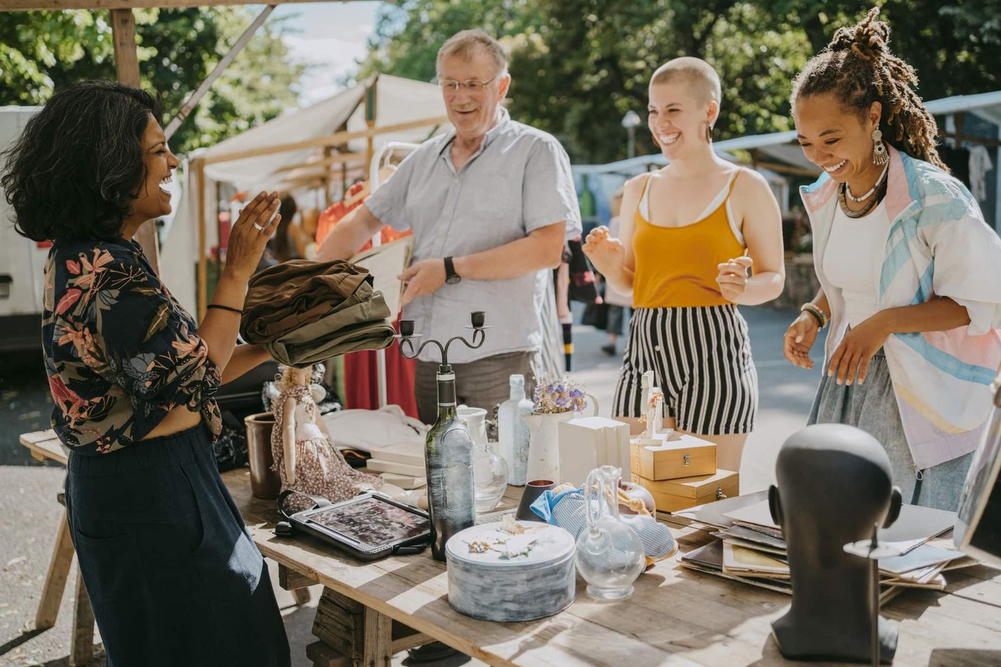 Gruppe von Menschen, die gemeinsam an einem Flohmarktstand Kleidung und Dekoartikel verkaufen. Getty