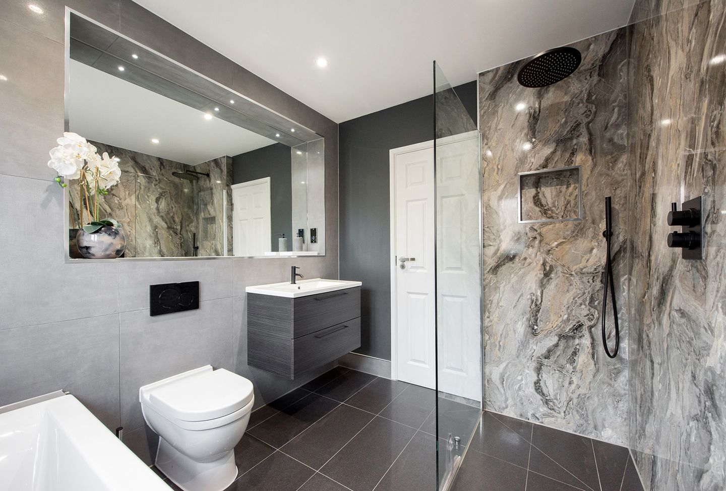 Ein modernes Badezimmer mit bodengleicher Dusche, Marmoroptik-Wand, Glasabtrennung, großem Spiegel und weißen Sanitärobjekten.