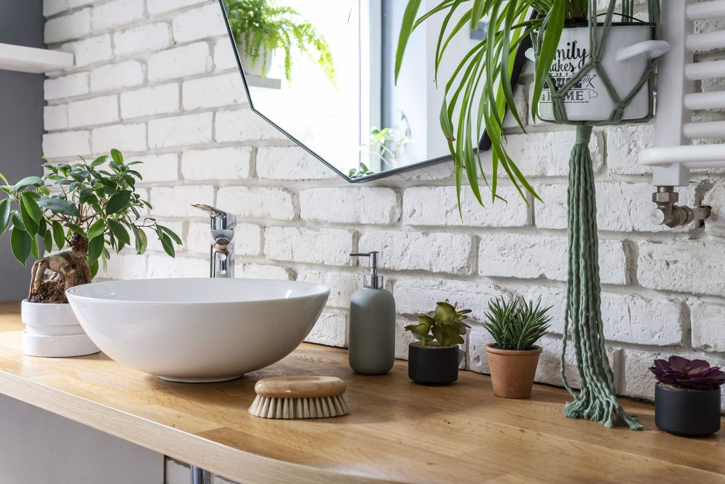 Badezimmer mit Naturmaterialien, weiß gestrichener Backsteinwand, Holzablage, Pflanzen und rundem Aufsatzwaschbecken. Getty
