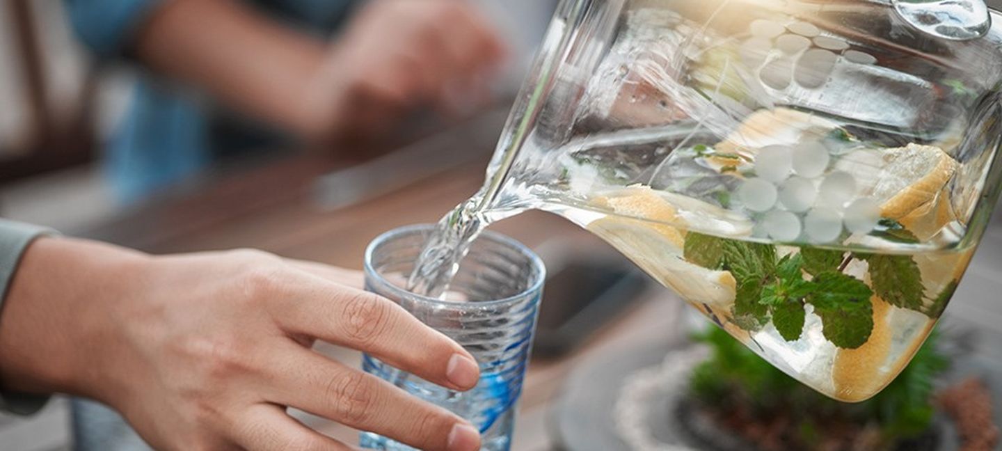 Wasser trinken: Einer Person wird Zitronenwasser mit etwas Minze in ein Glas geschüttet.