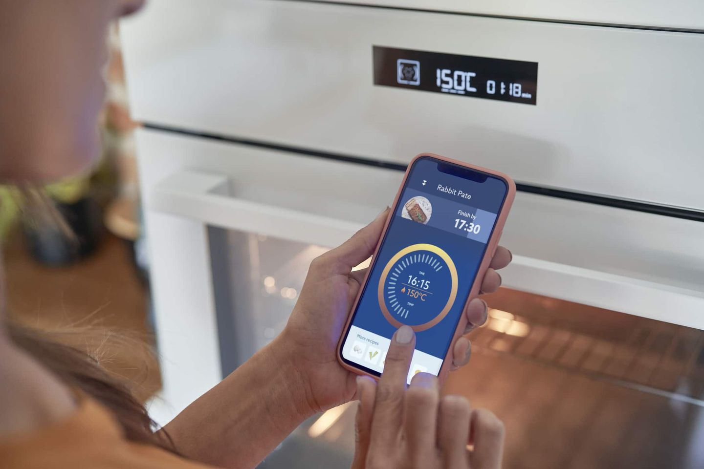Frau kontrolliert den Backofen mit einer Smart-Home-App auf dem Smartphone. Getty