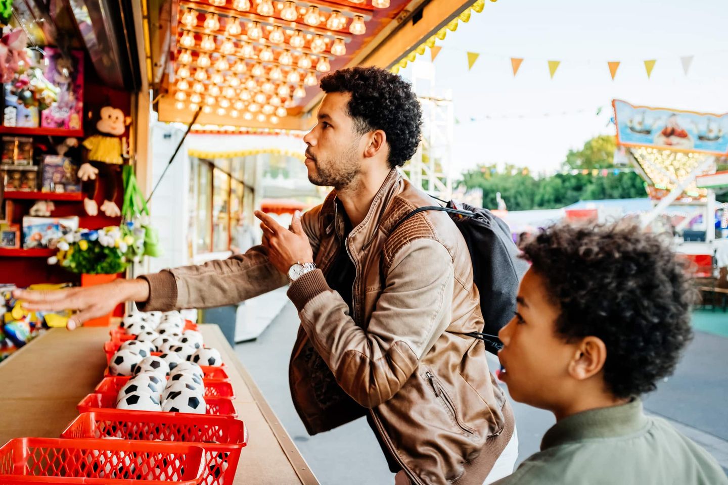 Vater und Sohn spielen ein Wurfspiel mit kleinen Fußbällen an einem Kirmesstand Getty