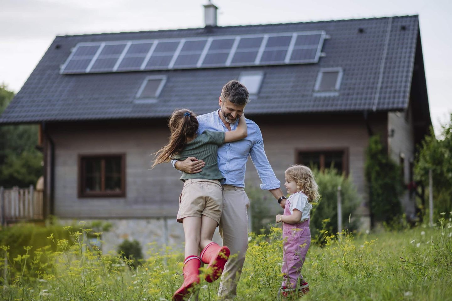Vater mit zwei Kindern im Garten vor einem Haus mit Solaranlage. Getty
