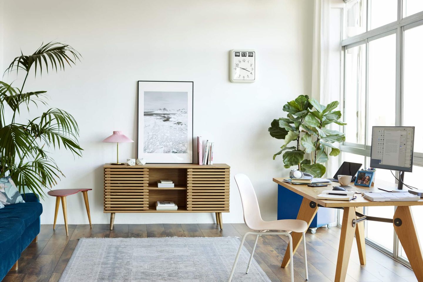 Helles, modern eingerichtetes Wohnzimmer mit Schreibtisch und großen Zimmerpflanzen. Getty