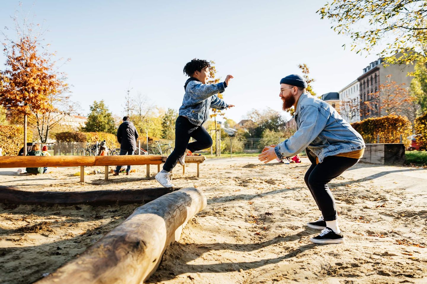 Ein Mann fängt auf einem Spielplatz ein Kind auf, das von einem Baumstamm springt. Getty