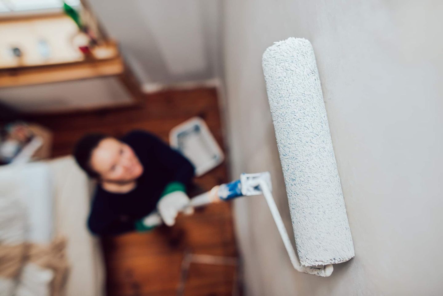 Frau streicht mit einer Farbrolle eine Wand weiß in einer Wohnung. Getty