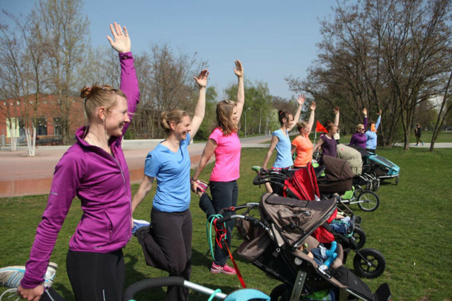 Frauen mit Kinderwagen machen Sport auf einer Wiese