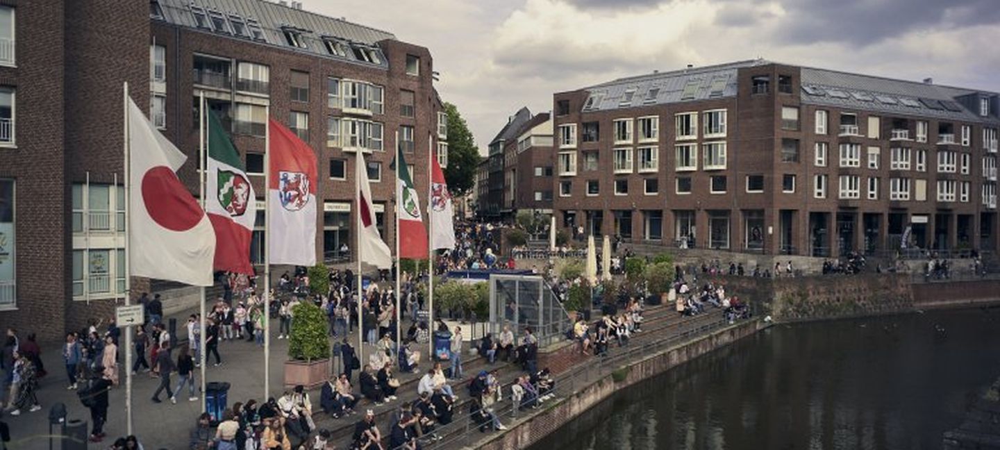 Blick auf den Alten Hafen in Düsseldorf mit Menschen am Wasser, Flaggen und Gebäuden Düsseldorf Tourismus GmbH