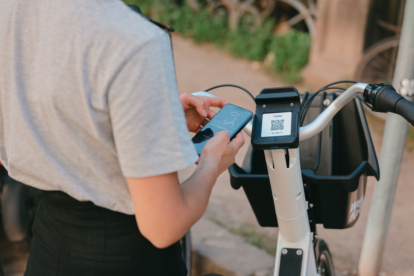 Person entsperrt ein weißes Düsselbike mit dem Smartphone; am Lenker ist der QR-Code des Fahrrads zu sehen. Connected Mobility Düsseldorf GmbH (CMD)