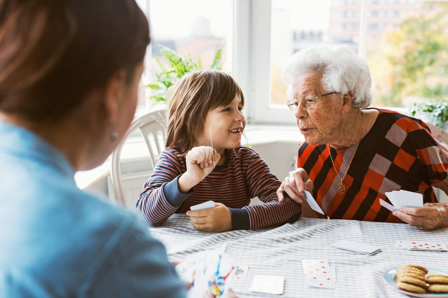 Eine ältere Frau spielt Karten mit einem Kind und einer weiteren Person am Tisch. Getty