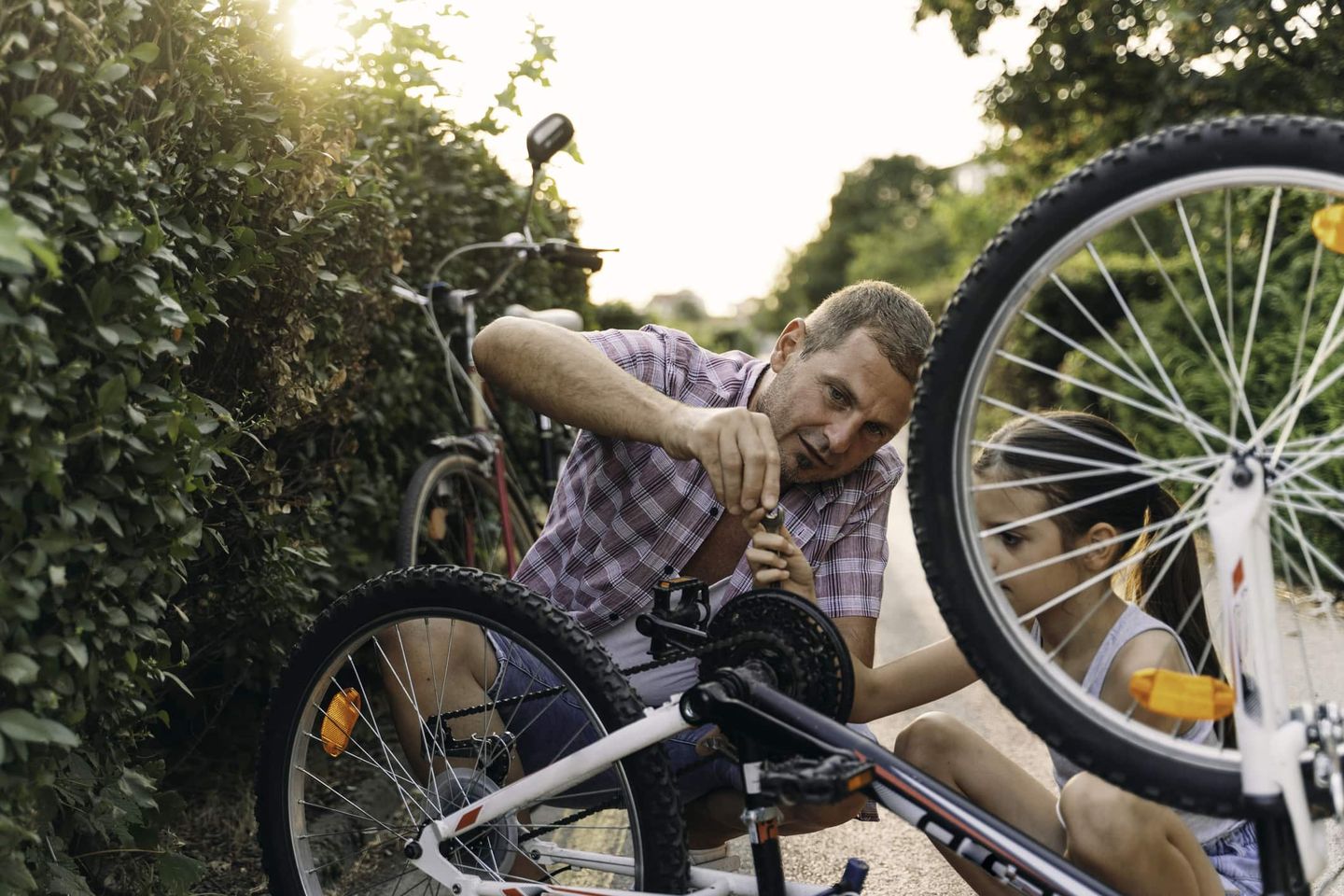 Vater und Tochter reparieren gemeinsam ein Fahrrad auf einem Weg im Grünen Getty