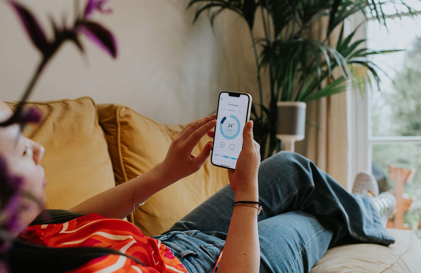 Frau steuert die Raumtemperatur mit Smart-Home-App auf dem Smartphone vom Sofa aus. Getty