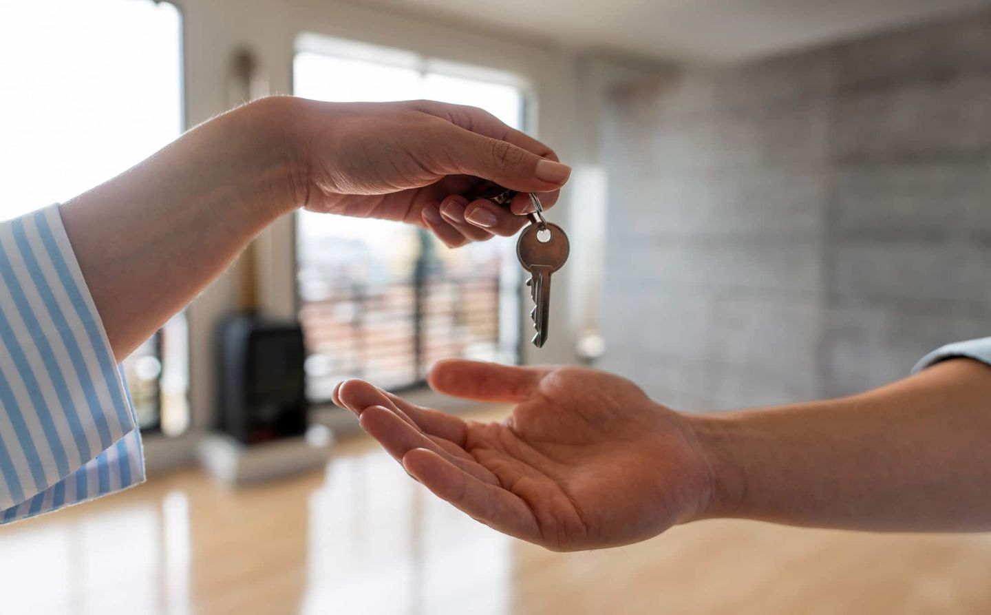 Eine Hand übergibt einen Wohnungsschlüssel an eine andere Hand in einem hellen Raum. Getty