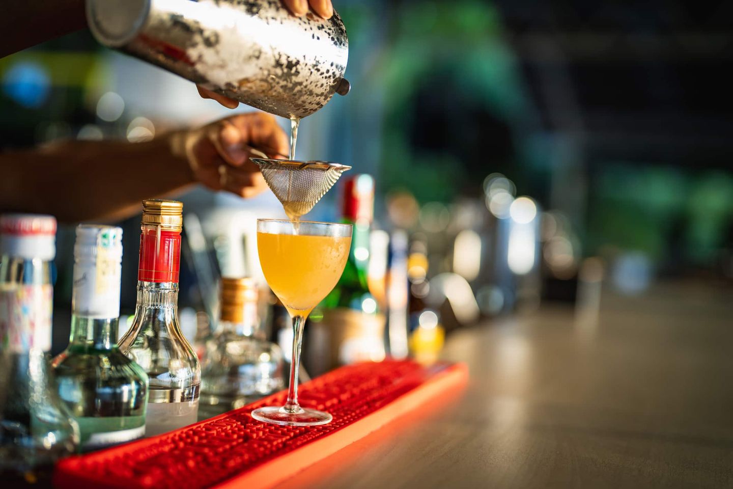 Ein Barkeeper gießt einen frisch gemixten Cocktail durch ein Sieb in ein Glas an der Bar. Getty