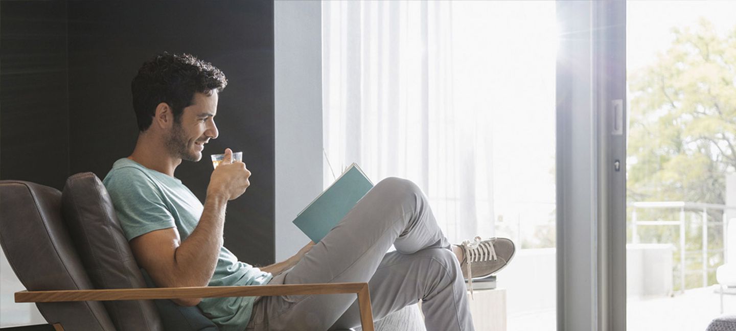 Ein junger Mann sitzt in einem Sessel, trinkt eine Tasse Tee und liest ein Buch