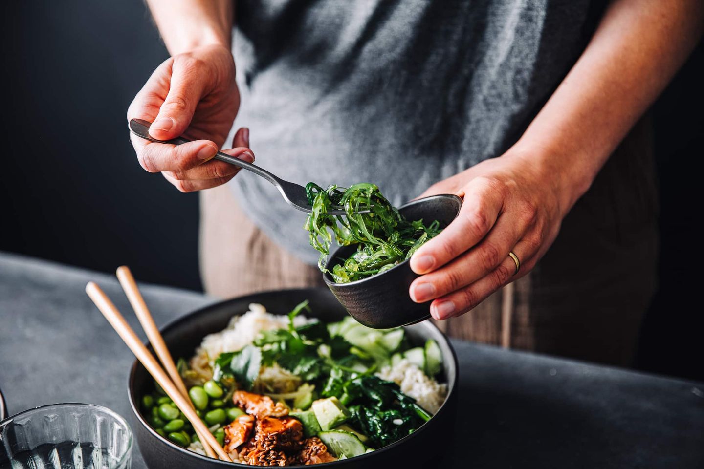 Person bereitet eine Poké Bowl mit frischem Gemüse und Fisch zu. Getty