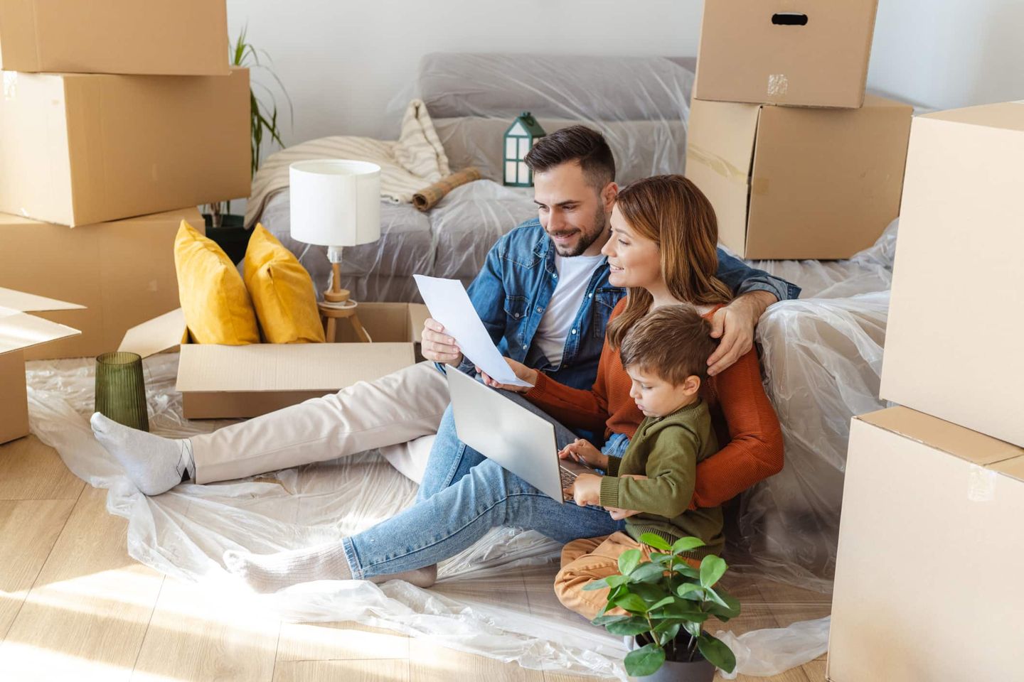 Eine Familie sitzt zwischen Umzugskartons im neuen Zuhause und schaut gemeinsam auf Unterlagen. Getty