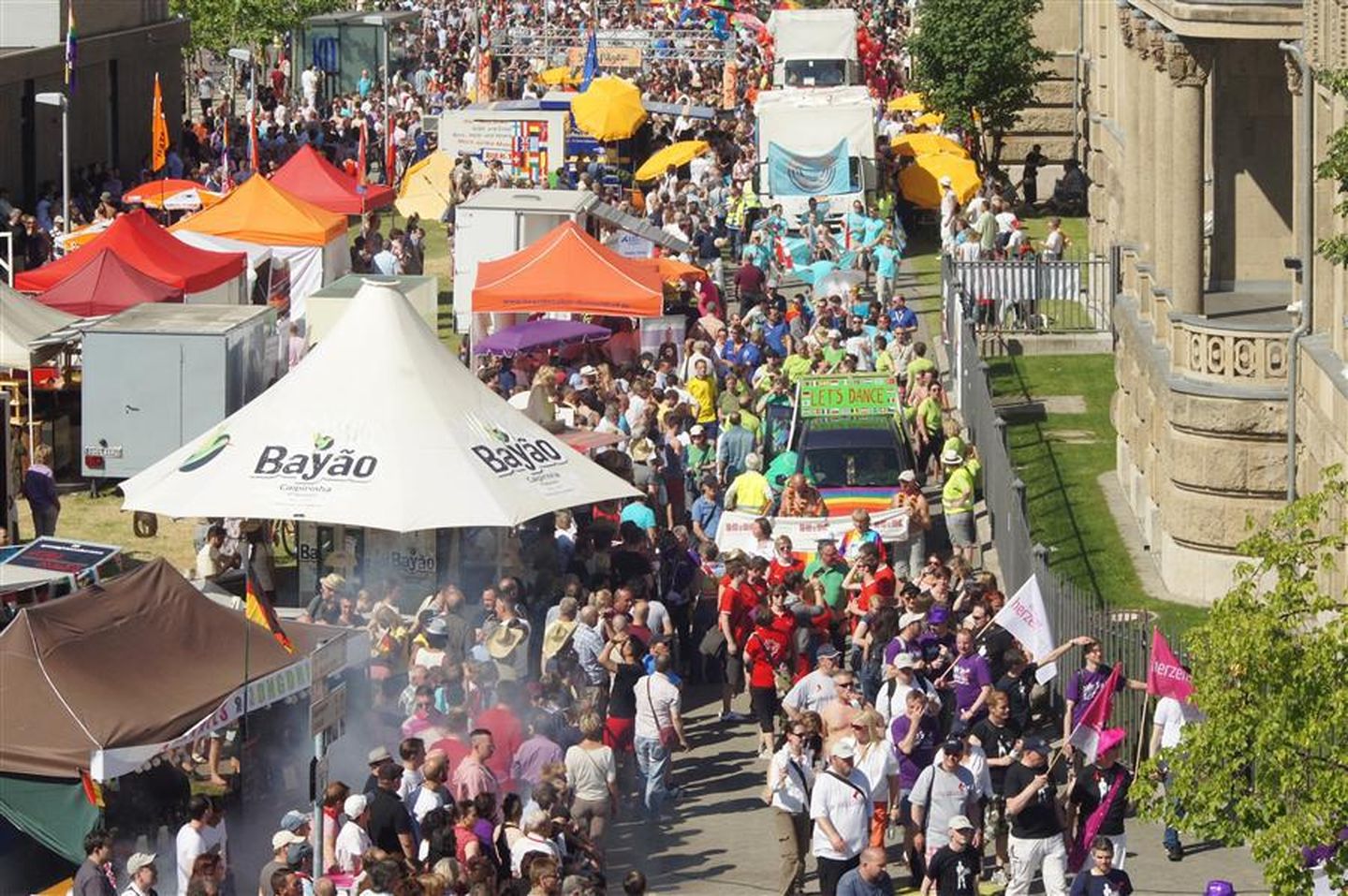 An diversen Ständen und Zelten schauen Menschen der CSD-Demo in Düsseldorf zu.  © CSD Düsseldorf e. V.