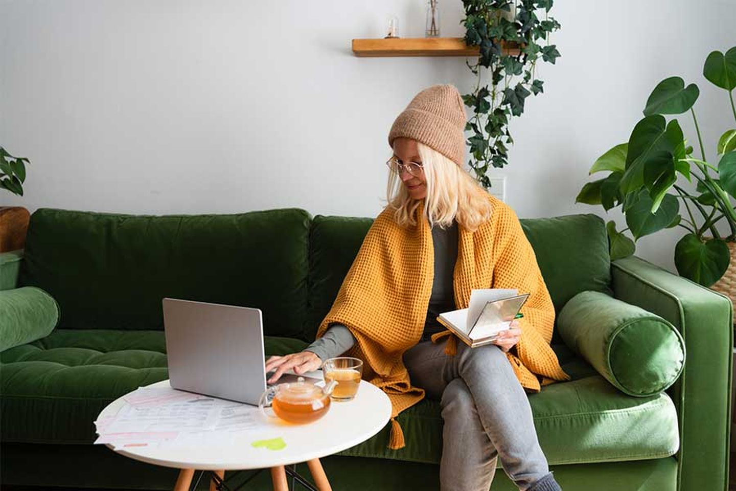 Eine Frau sitzt auf der Couch und verschafft sich mithilfe von Computer und Notizen einen Überblick über ihre Heizkosten. © ingwervanille / Moment via Getty Images