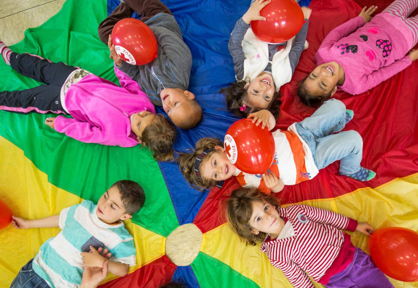 Mehrere Kinder liegen auf dem Boden und spielen mit Luftballons des DRK.