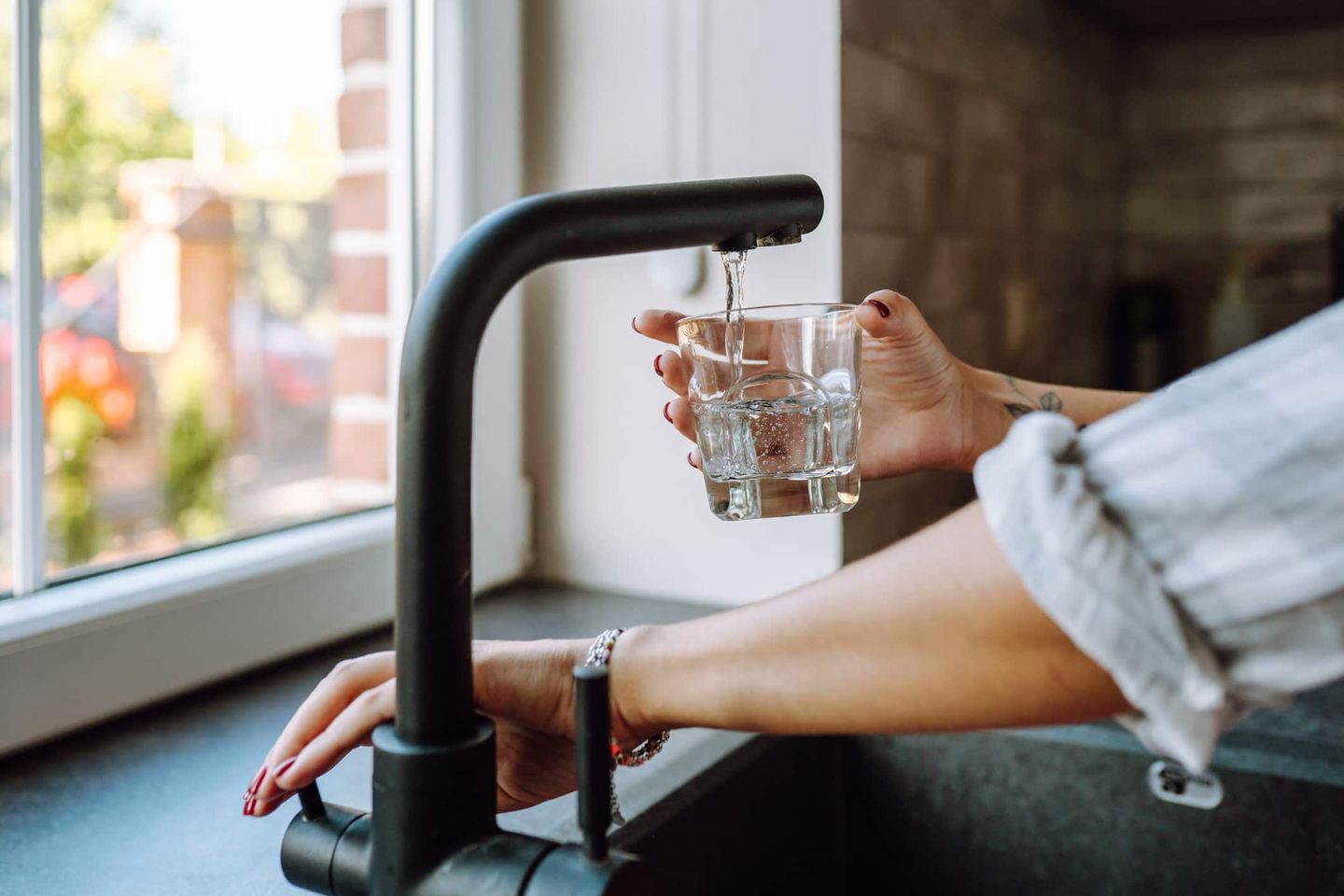Eine Person füllt ein Glas mit frischem Leitungswasser aus der Küchenarmatur. Getty