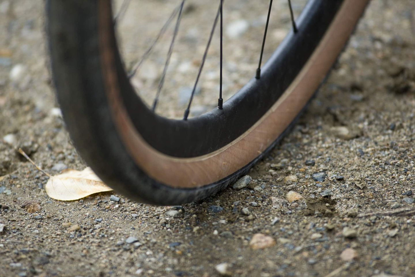 Nahaufnahme eines Fahrradreifens auf kiesigem Untergrund, bei der der Fokus auf den Speichen des Vorderrads liegt.