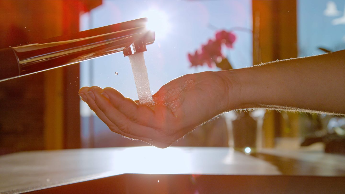 Hand unter fließendem Wasserhahn im Sonnenlicht Getty
