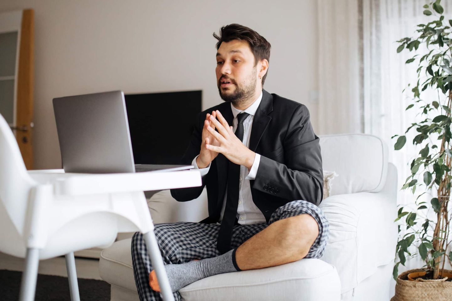 Mann im Anzugjackett und Pyjamahose sitzt vor Laptop im Homeoffice. Getty