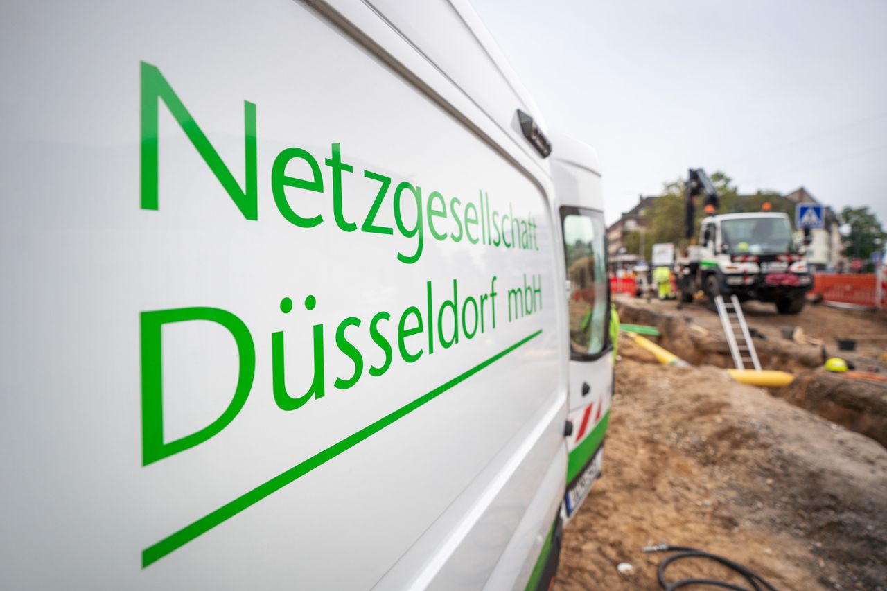 White van with "Netzgesellschaft Düsseldorf mbH" parked near a construction site with workers and machinery in the background.