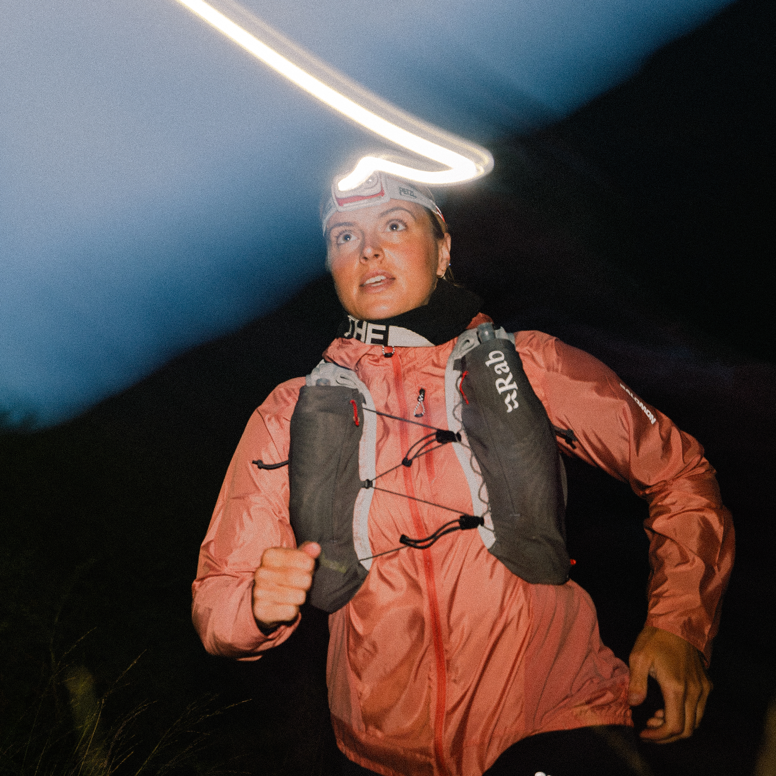 Night trail runner with headlamp and hydration vest, focused and determined, against a dark mountain backdrop.