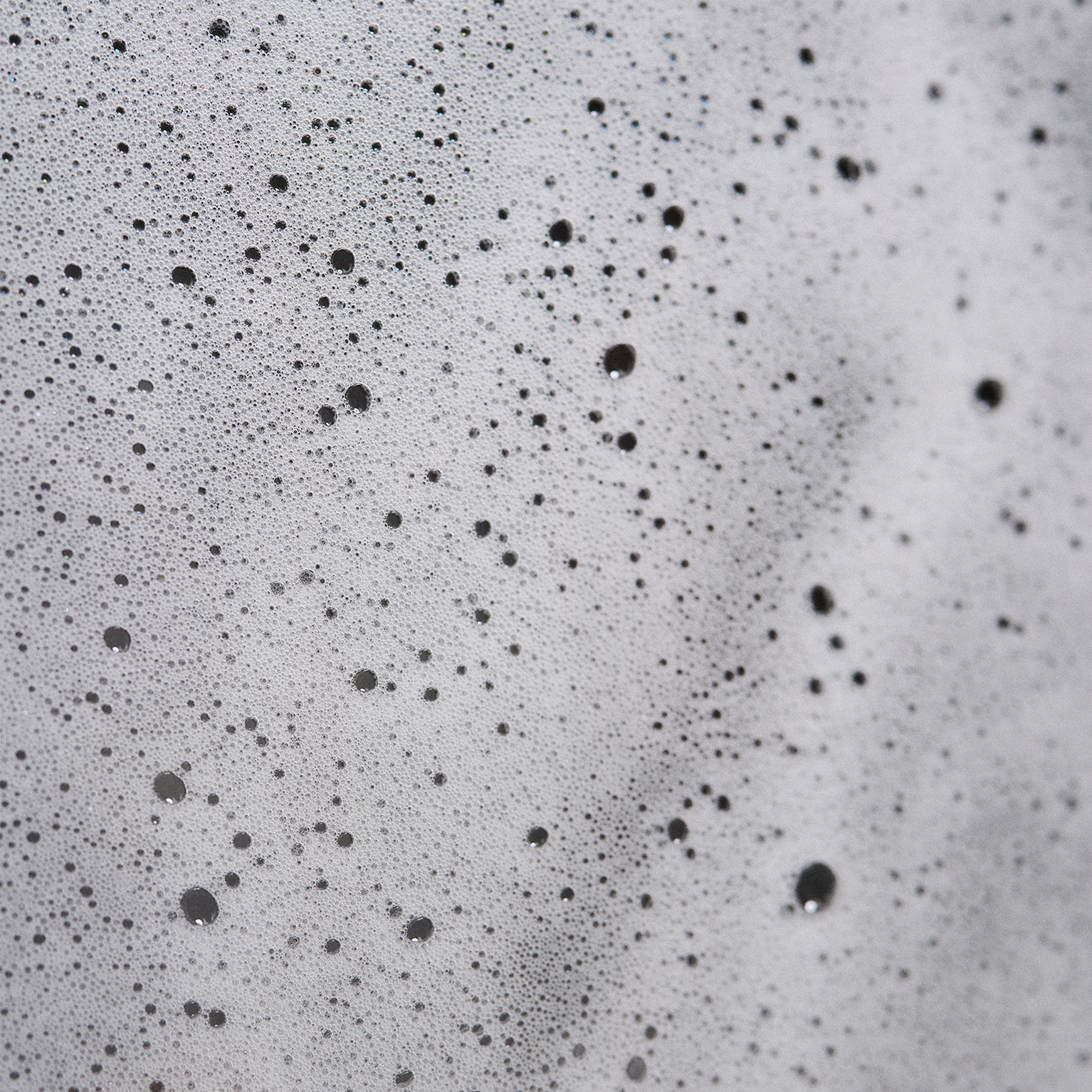 Close-up of soap bubbles forming a foamy texture with various-sized bubbles on a smooth surface, creating a speckled pattern.