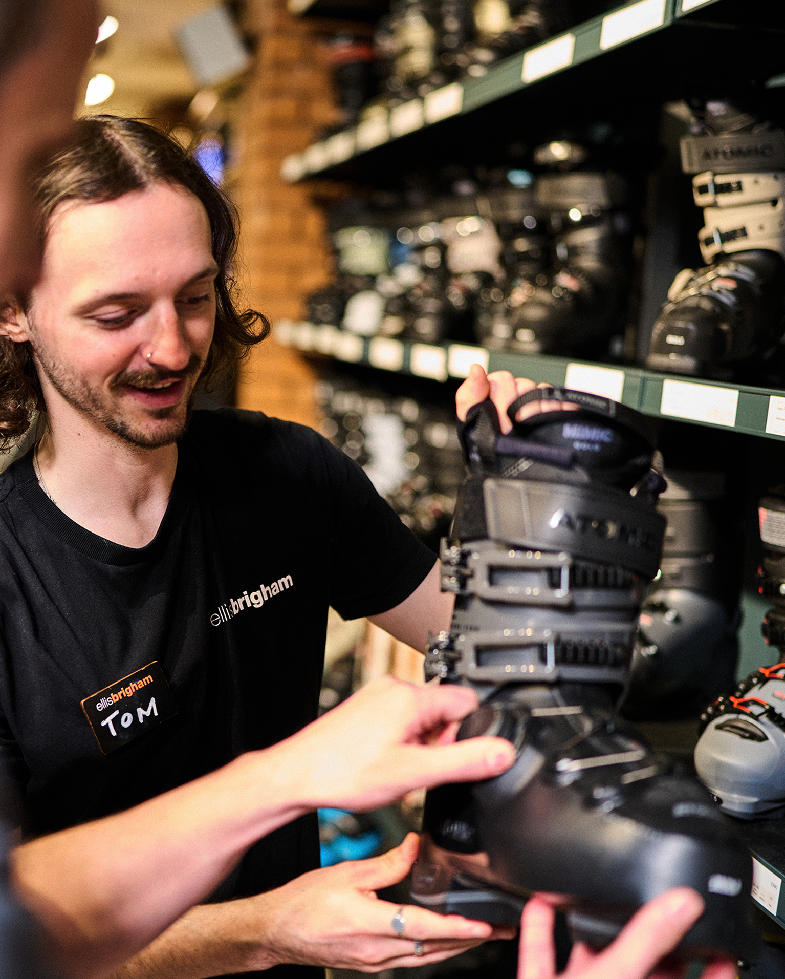 An employee assisting a customer with selecting ski boots in a mountain sports store.