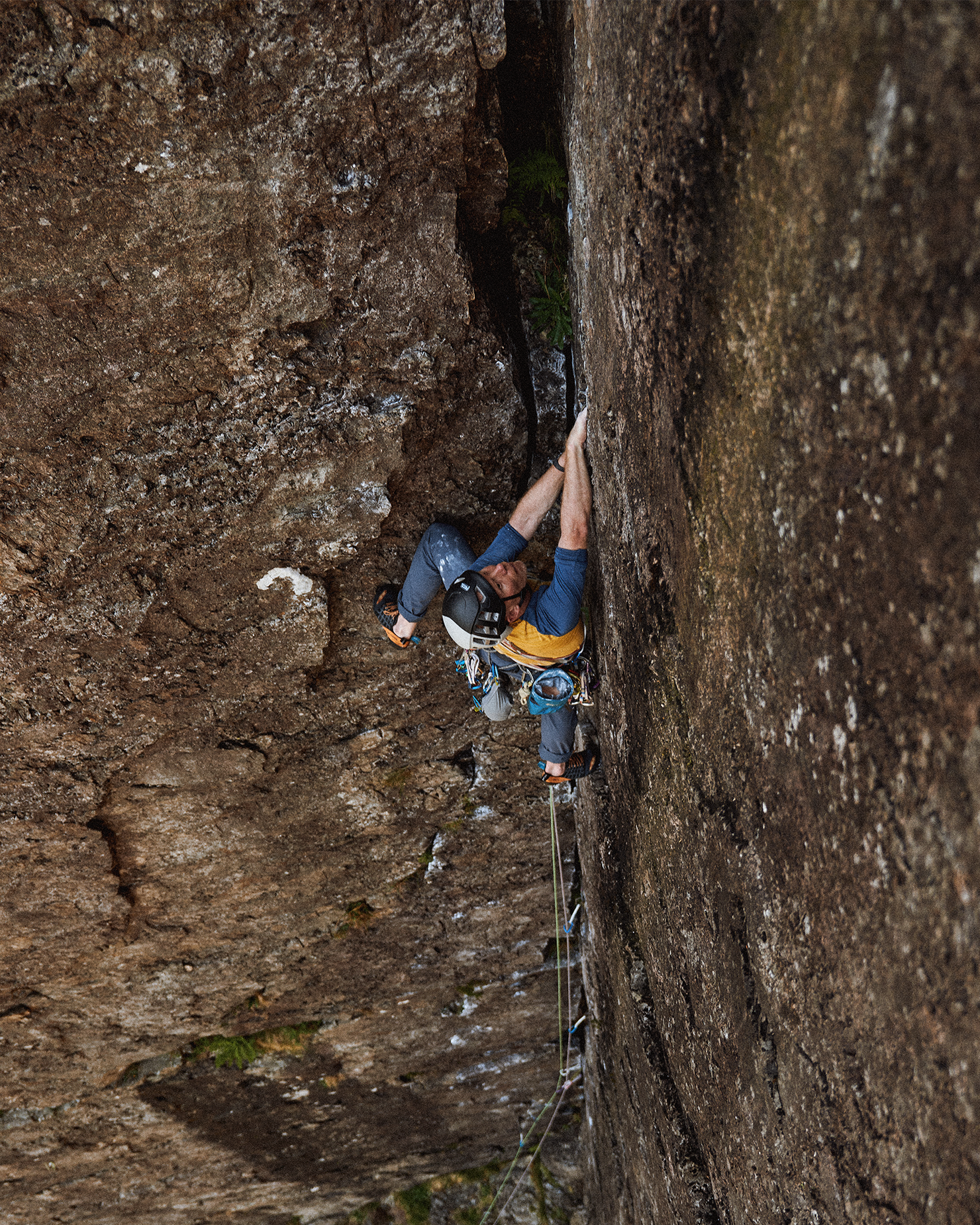 Climber ascends steep rock face using ropes and gear, against a rugged cliff background.