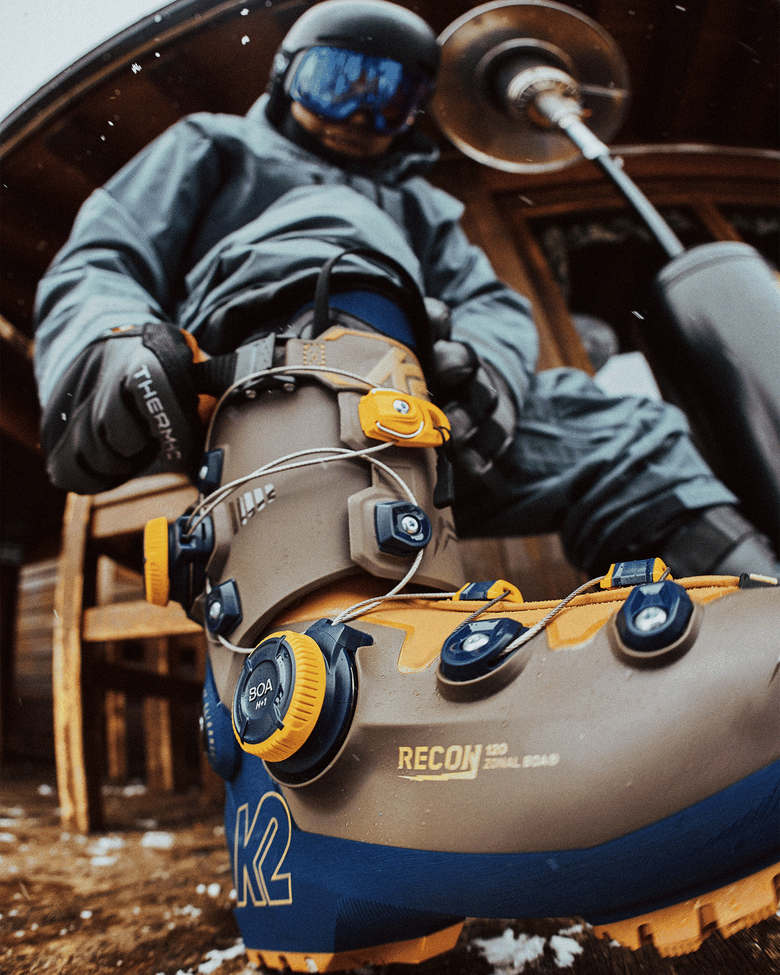 Person adjusting ski boots, featuring secure fastenings and rugged design, outside a wooden lodge.