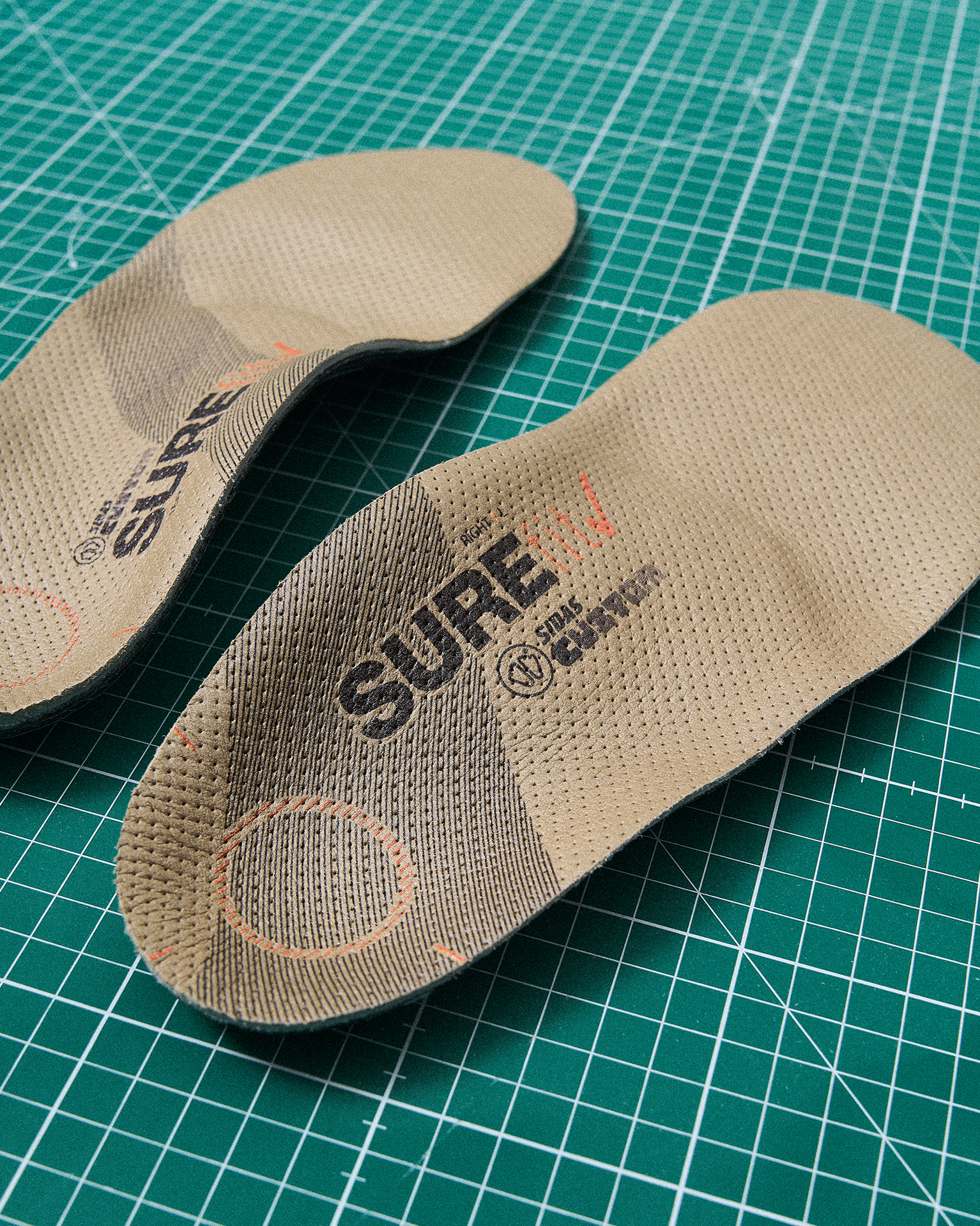Pair of brown insoles on a green cutting mat, featuring branding and textured surface for comfort.